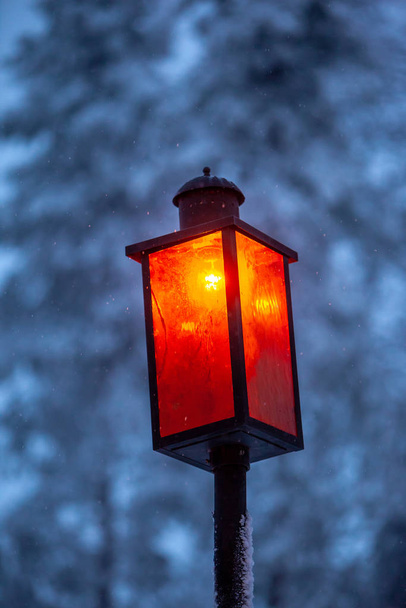 Уютная винтажная уличная лампа, покрытая снегом на заднем плане под открытым небом при снегопаде. Ретро-металлическое украшение фонаря на альпийской курортной улице. Рождественская сцена
 - Фото, изображение