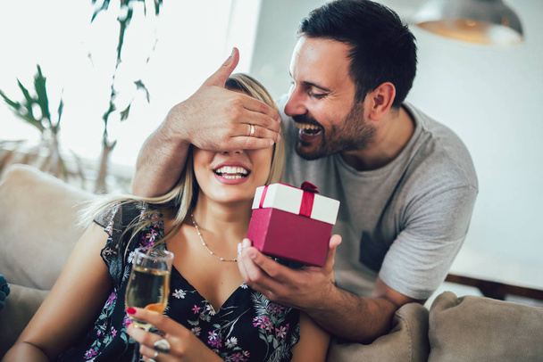 Young man giving a surprise gift to woman in the living room at  - Photo, Image