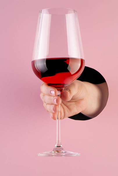 Hand holds a glass of rose wine through a hole in paper pink bac - Foto, Imagem