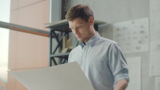 Hipster engineer works with blueprint. Shoot from above. Young architectural engineer working in office. Bearded man makes sketches. Loft style, minimalistic interior, drawings on the table. - Záběry, video