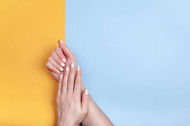 Piękne kobiece dłonie z klasycznym matowym manicure na niebiesko-żółtym tle - Zdjęcie, obraz