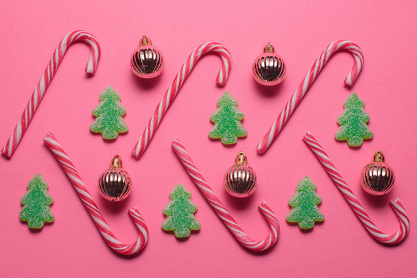 Candies in the shape of a Christmas tree and golden balls lie on a pink background, top view. - Fotografie, Obrázek