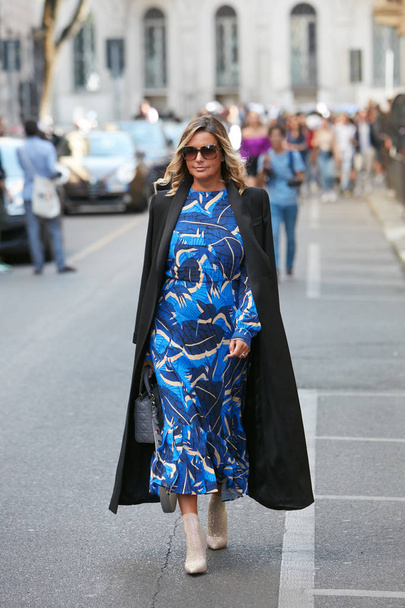 Woman with blue tones dress and long black coat before Giorgio Armani fashion show, Milan Fashion Week street style  - Foto, imagen