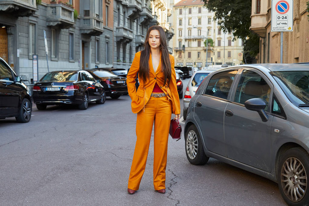 Woman with orange jacket and trousers before Salvatore Ferragamo fashion show, Milan Fashion Week street style  - Foto, afbeelding