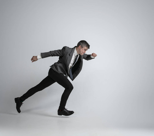 Caucasian man in office clothes running isolated on grey studio background - Фото, зображення