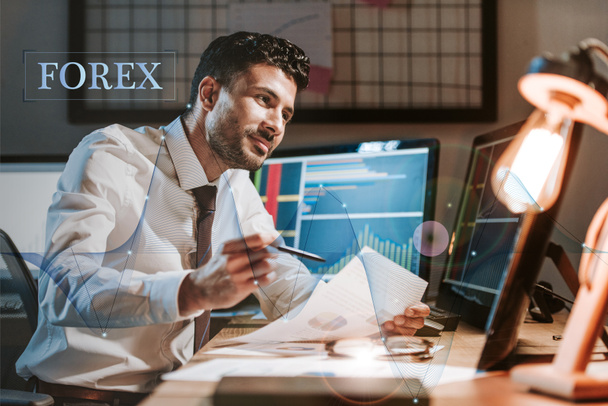 happy bi-racial trader holding paper near computer with graphs and forex letters - Photo, Image