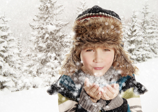 Onnellinen poika puhaltaa lumihiutaleita talvimaisemassa
 - Valokuva, kuva