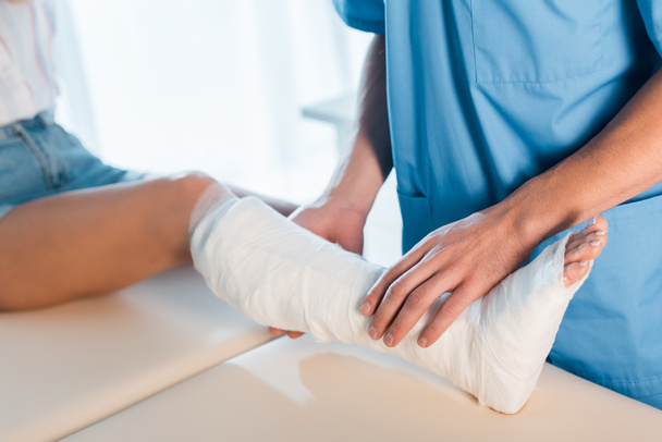 przycięty widok ortopedy dotykającej złamanej nogi kobiety  - Zdjęcie, obraz