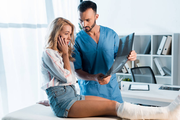 handsome orthopedist and shocked woman looking at x-ray  - Zdjęcie, obraz