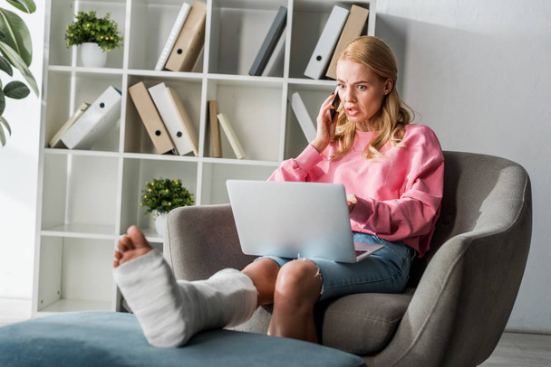injured woman talking on smartphone while working from home  - Foto, afbeelding