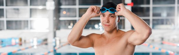 panoramic shot of happy athletic swimmer touching goggles  - Foto, Imagen