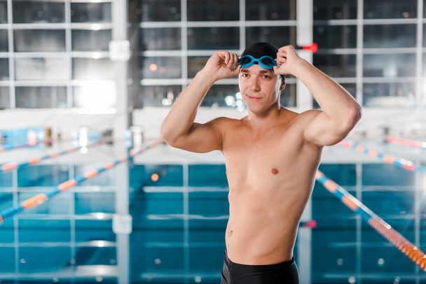 nadador atlético feliz tocando gafas cerca de la piscina
  - Foto, Imagen