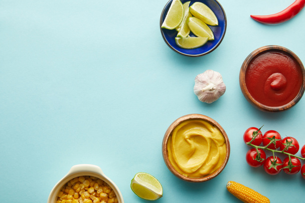 Top view of lime, mustard with tomato sauce and vegetables on blue background - Foto, afbeelding