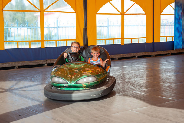 Dzieci jeżdżą elektrycznymi samochodami w parku rozrywki. - Zdjęcie, obraz