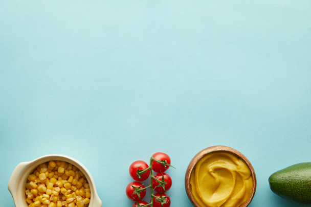 Horní pohled na kukuřici, hořčici s avokádem a cherry rajčata na modrém pozadí s kopírovacím prostorem - Fotografie, Obrázek