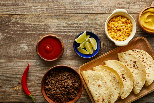 Top view of fresh tortillas with sauces and ingredients on wooden background - Foto, imagen