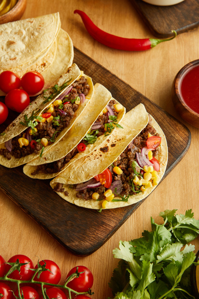 Top view of tacos on cutting board with ripe vegetables on wooden table - Photo, Image