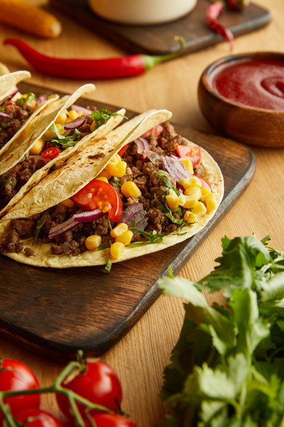 Tasty tacos on cutting board with fresh vegetables on wooden background - Valokuva, kuva