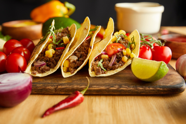 Focus selettivo di tacos freschi con ingredienti su tavolo in legno su sfondo nero
 - Foto, immagini
