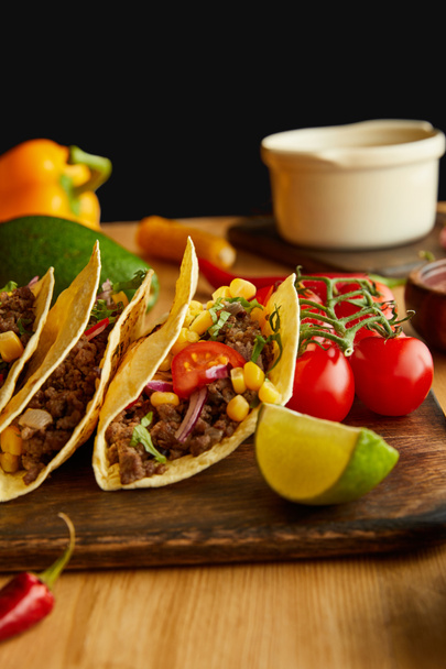 Tasty tacos with lime and cherry tomatoes on wooden table on black background - Photo, image