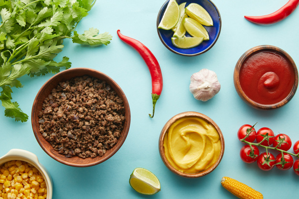 Top view of organic vegetables with sauces and minced meat on blue background - Foto, afbeelding