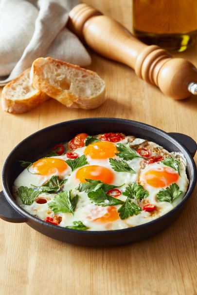 fried eggs with parsley and chili pepper on wooden table with bread - Photo, image