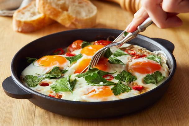 cropped view of eating fried eggs with parsley and chili pepper on wooden table with fork and knife - Photo, Image