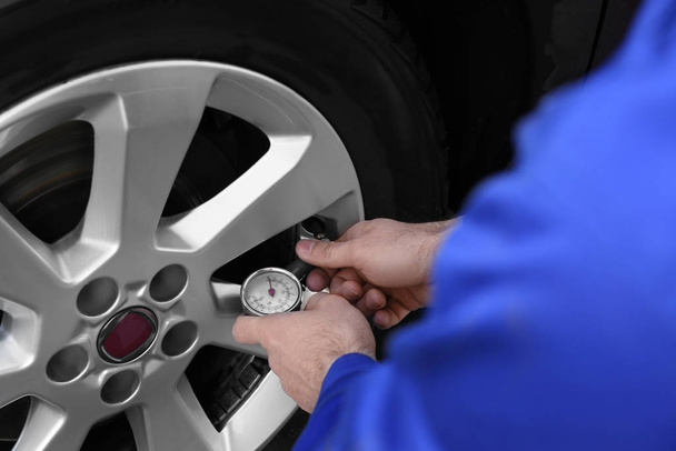 Механик проверяет давление воздуха в шинах при обслуживании автомобилей, крупный план
 - Фото, изображение