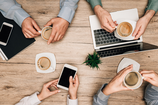 Top view of business partners drinking coffee by gadgets on table, cropped view - Fotó, kép