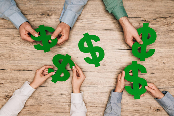 Top view of businesspeople holding dollar signs at wooden table, cropped view - Foto, imagen
