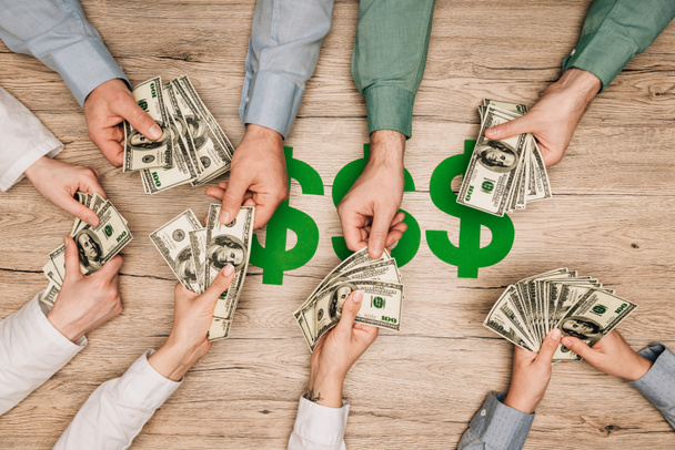 Top view of business partners holding dollar banknotes with dollar signs on table, cropped view - 写真・画像