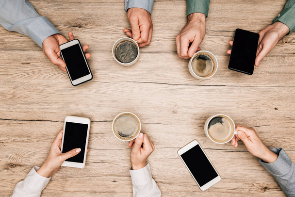 Vista dall'alto degli uomini d'affari che bevono caffè e usano gli smartphone al tavolo di legno, vista ritagliata
 - Foto, immagini