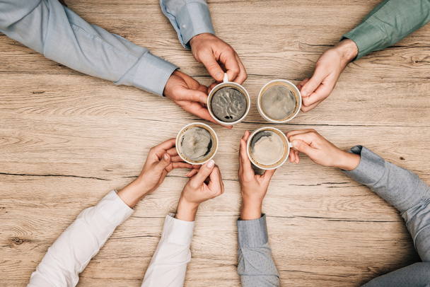 Top view of colleagues drinking coffee at wooden table, cropped view  - Foto, imagen