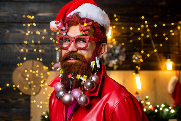 Santa otec s bílým vousem pózuje na vánočním dřevěném pozadí. Vousatý muž se baví poblíž vánočního stromečku. Nový rok vánoční koncept. - Fotografie, Obrázek