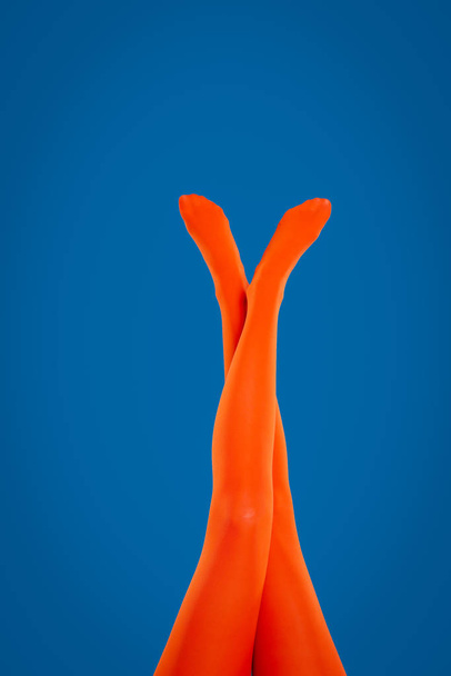 Woman wearing orange tights on blue background, closeup of legs - Photo, Image