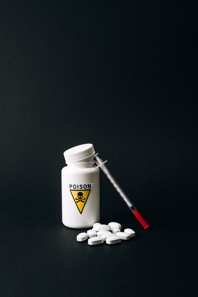 Jar with poison sign with pills and syringe isolated on black - Valokuva, kuva