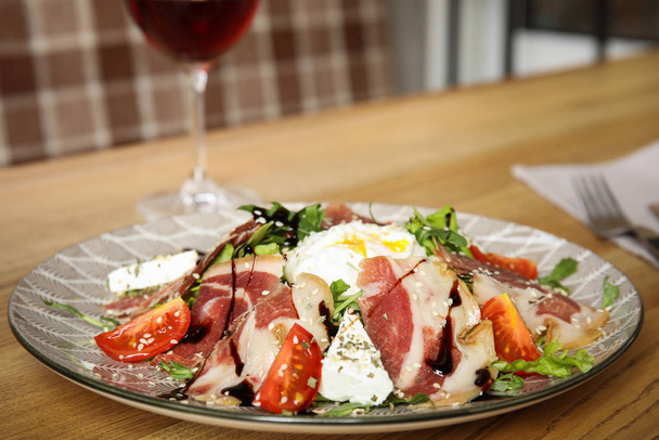 Delicious prosciutto salad with vegetables served on wooden table indoors - Photo, image