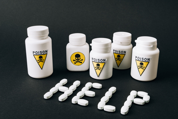 Jars with poison sign and help lettering from pills isolated on black - 写真・画像