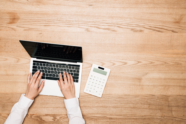 Widok z góry businesswoman za pomocą laptopa przez kalkulator na drewnianym stole, widok przycięty - Zdjęcie, obraz