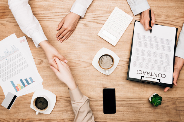 Top view of business partners shaking hands near contract, coffee and credit card on table - Zdjęcie, obraz
