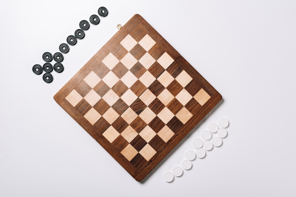 Bovenaanzicht van houten schaakbord en dammen op witte achtergrond  - Foto, afbeelding