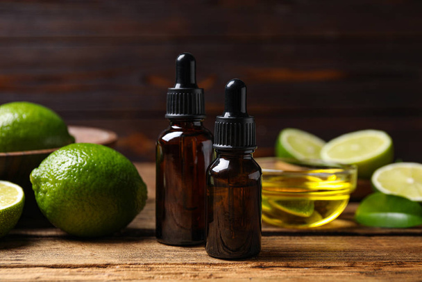 Lime essential oil and cut citrus fruits on wooden table - Fotó, kép