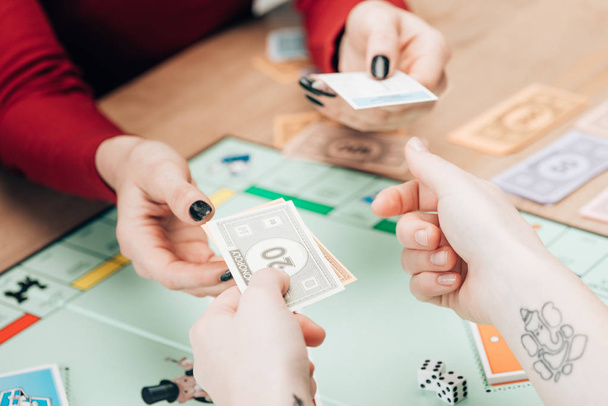 KYIV, UKRAINE - NOVEMBER 15, 2019: Cropped view of women with toy currency and cards playing in monopoly - 写真・画像