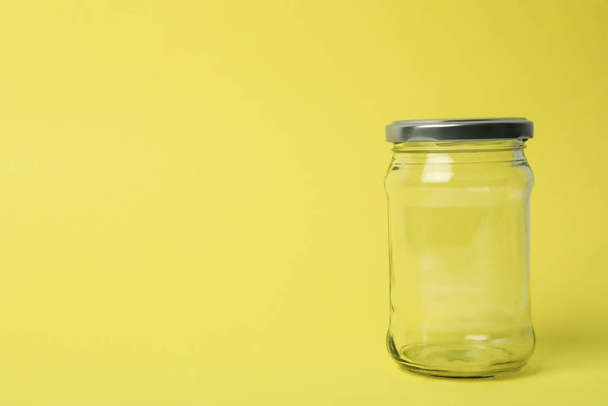 Closed empty glass jar on light yellow background, space for tex - Foto, afbeelding