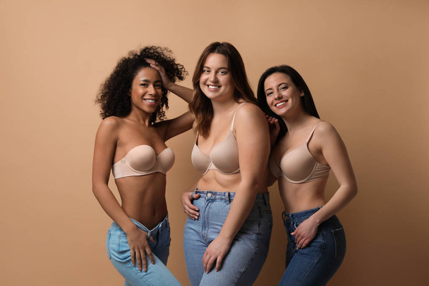Group of women with different body types in jeans and underwear on beige background - Foto, imagen