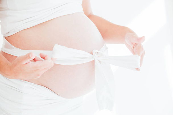 a pregnant womans belly and white bow gift - Photo, Image
