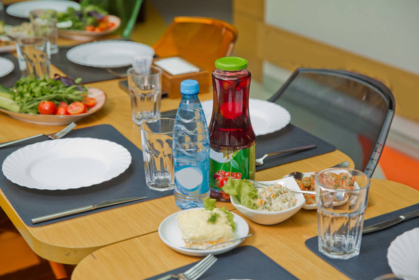 Tenedor de placa, cuchillo, vidrio. Bebida Kampot. Pepino de tomate y ensalada de bistec. Una mesa para niños en el restaurante
. - Foto, imagen