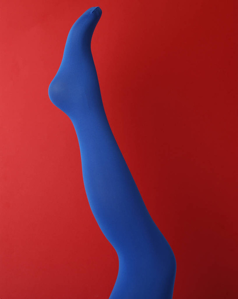 Leg mannequin in blue tights on red background - 写真・画像