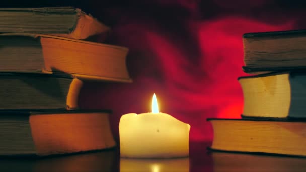 Στύλοι από βιβλία στέκονται δίπλα σε ένα αναμμένο κερί και ο μαύρος μαγικός καπνός πετάει.. - Πλάνα, βίντεο
