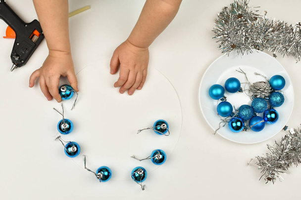 子供の手はクリスマスのおもちゃを作る。銀のチンセルとバンプ、クリスマスブルーボール. - 写真・画像